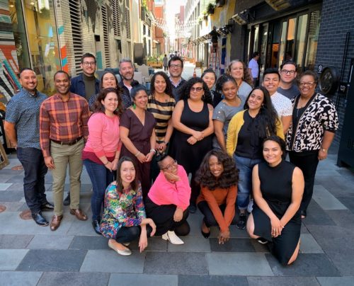 A group of 20 arts leaders of color smiling and posing on an outdoor street