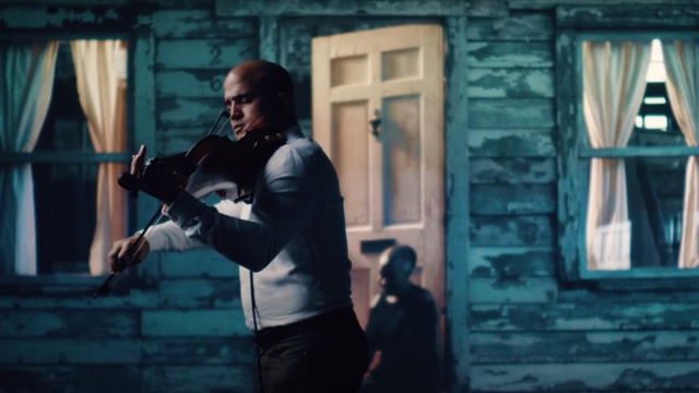 Man playing violin in front of a gloomy blue background.