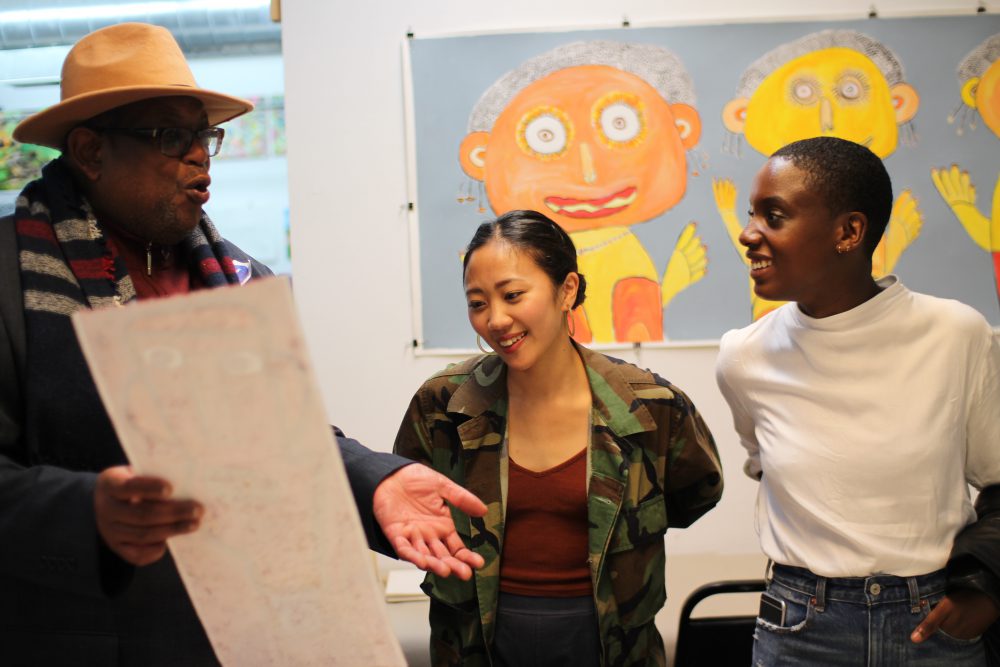 Creativity Explored artist Vincent Jackson shows off one of his artworks to two women visiting the studio.