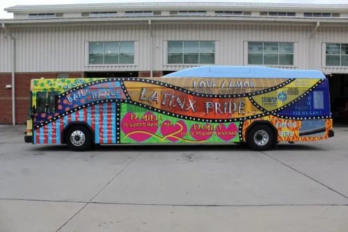 A bus covered in a vibrant multicolored wrap that reads Latinx Pride